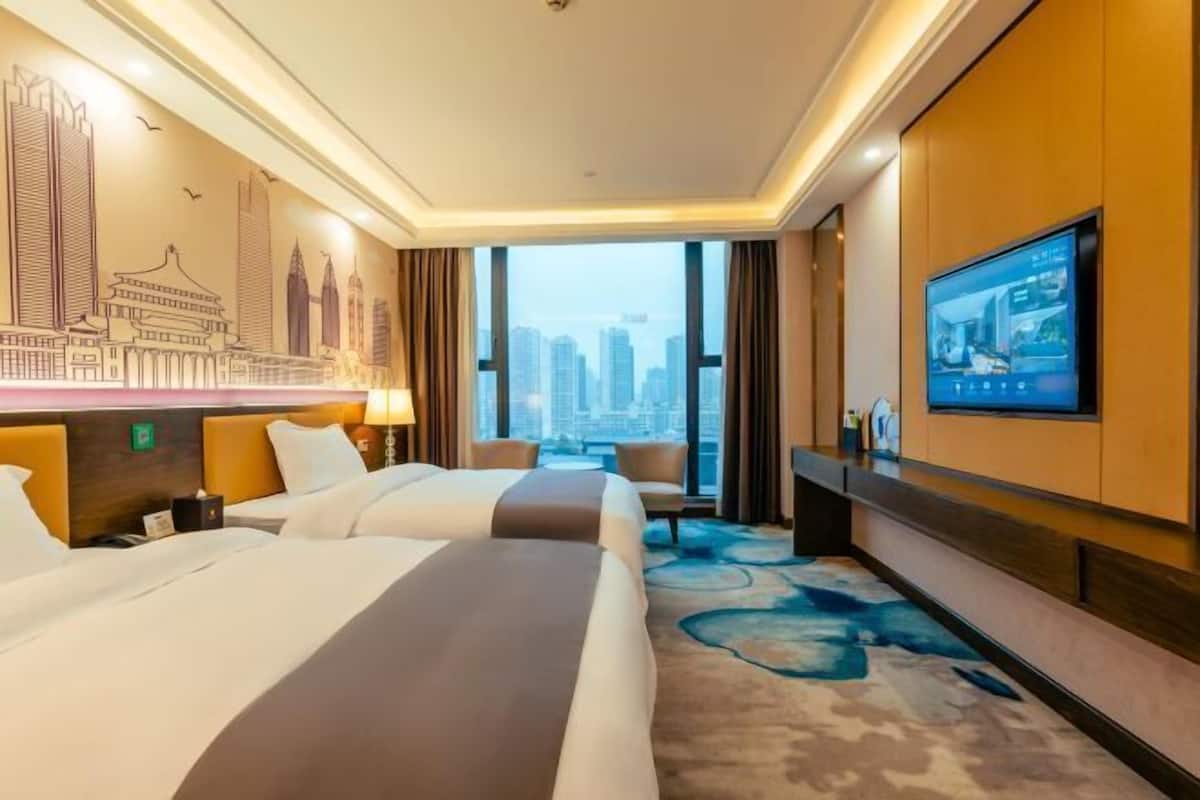 A hotel room with two beds, a large window with a city view, a television, and a wall mural.