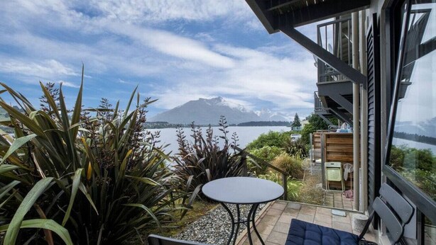 Un patio con tavolo e sedie, vista su un lago e montagne.