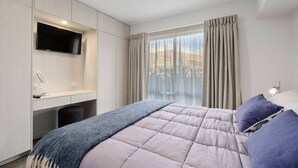 Una camera da letto moderna con un letto, una scrivania, una televisione e una finestra con tende.