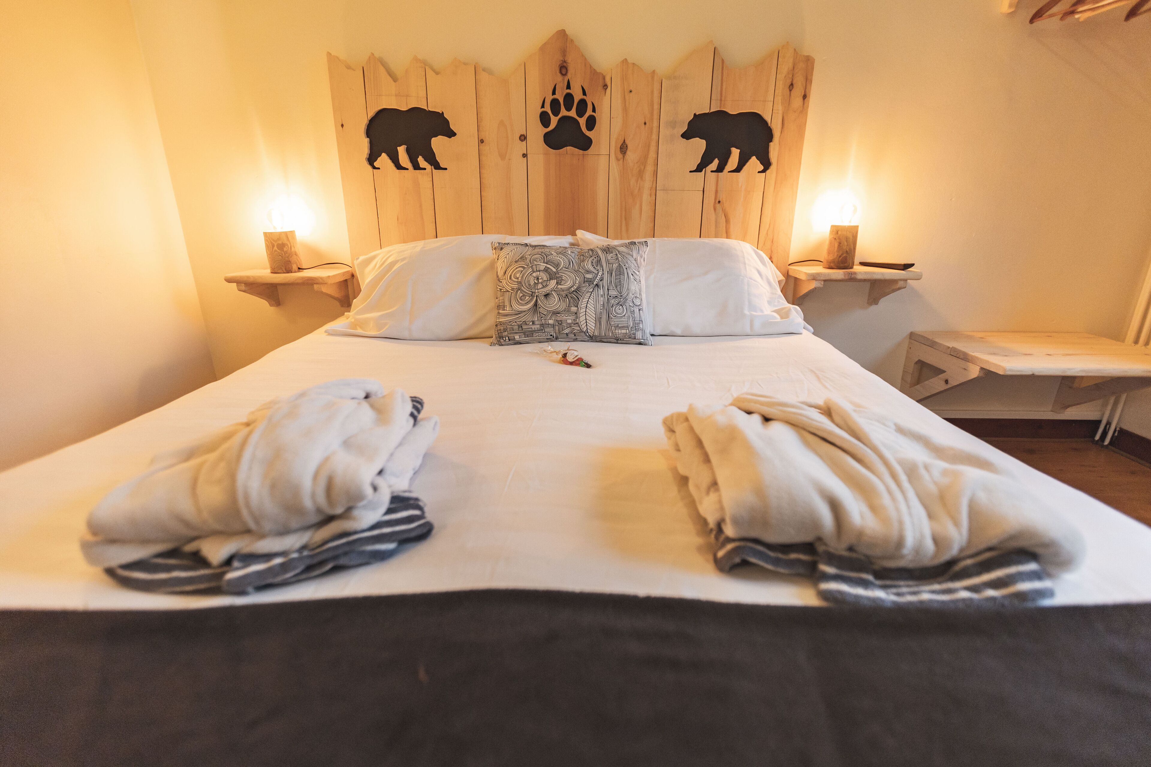 Una cama con dos toallas, un cojín decorativo y un cabecero de madera con siluetas de animales.
