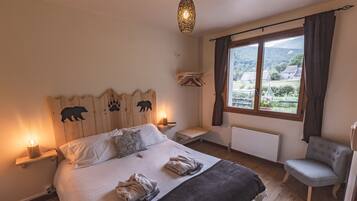 Un dormitorio con una cama grande, lámparas de noche, una ventana con vistas al campo, un cabecero de madera con siluetas de animales y un sillón gris.