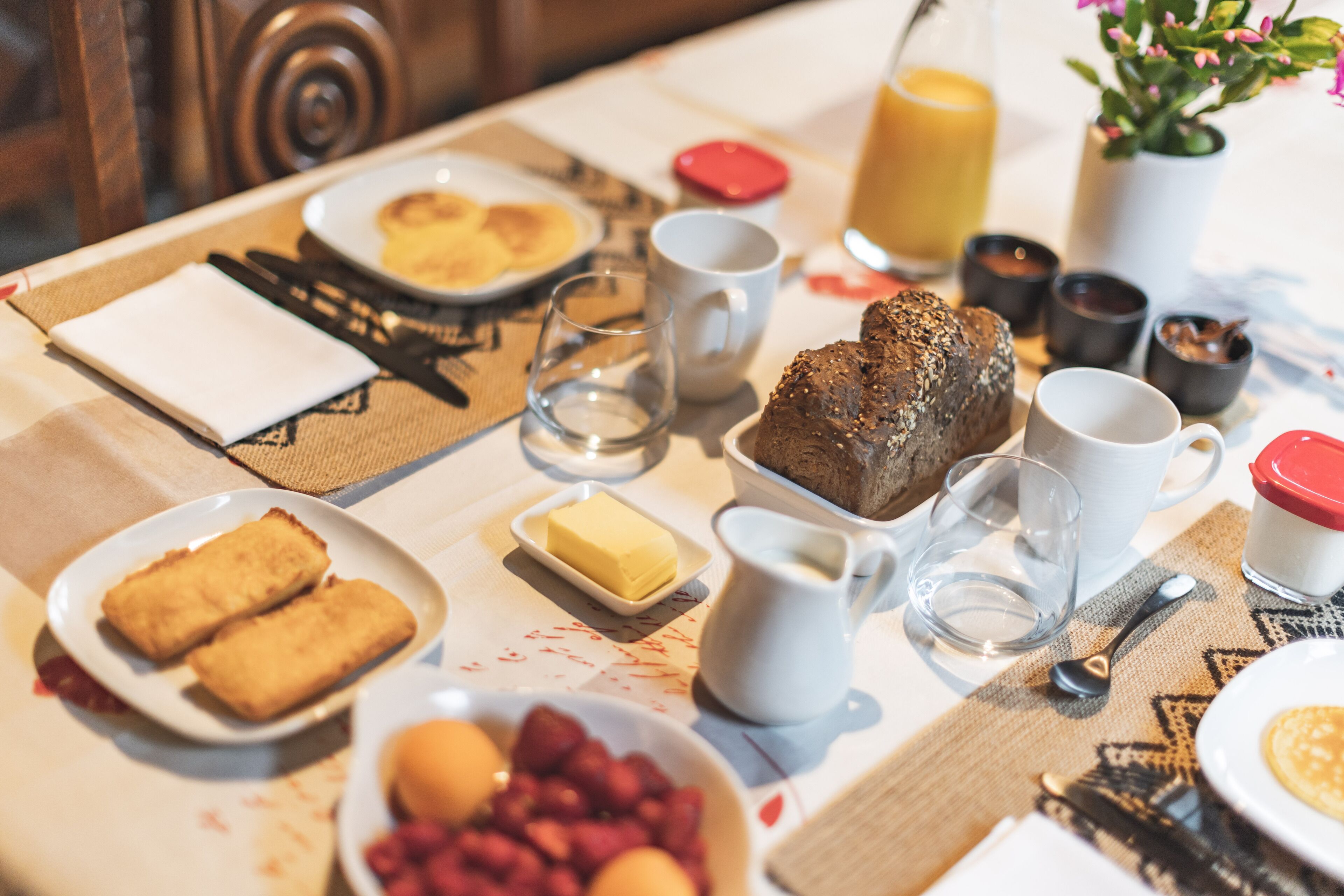 Une table de petit-déjeuner avec des assiettes remplies de nourriture, une carafe de lait et un verre de jus d’orange.