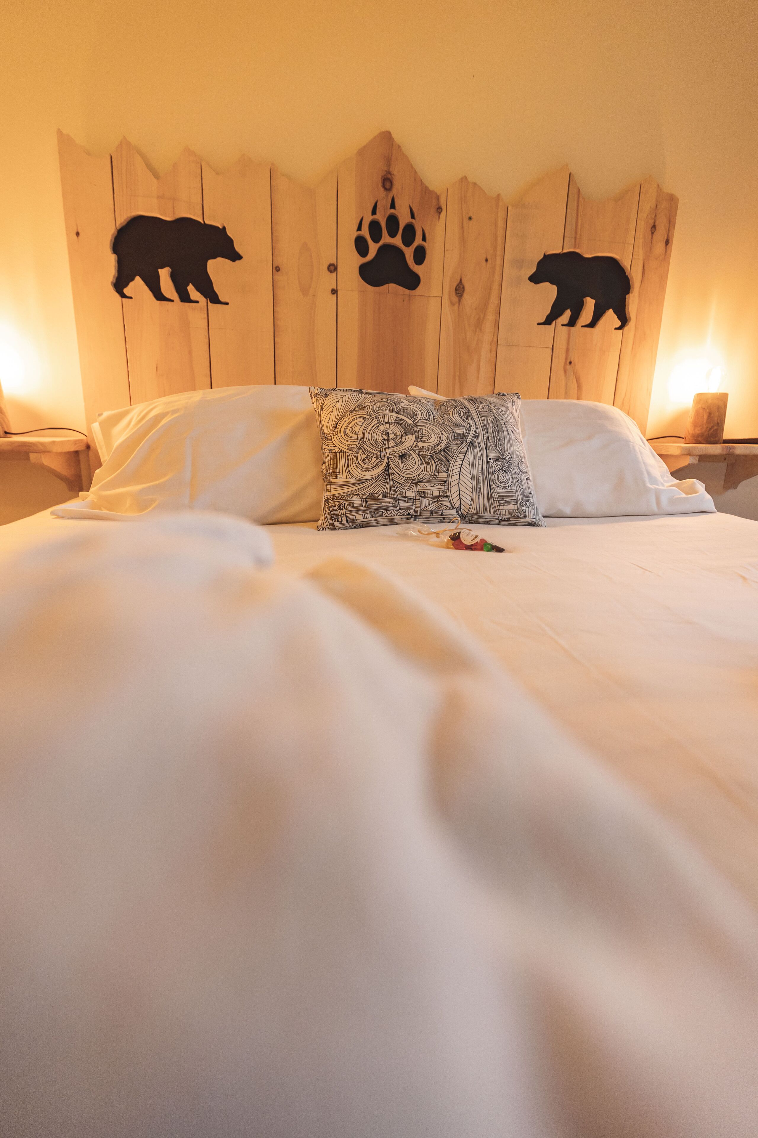 A bed with white bedding, a patterned pillow, and wooden headboard with bear and paw prints.