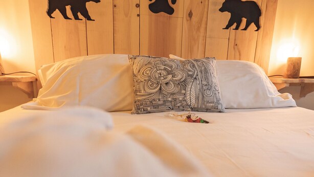 A bed with white bedding, a patterned pillow, and wooden headboard with bear and paw prints. - Chalet Ouréa (Campan)