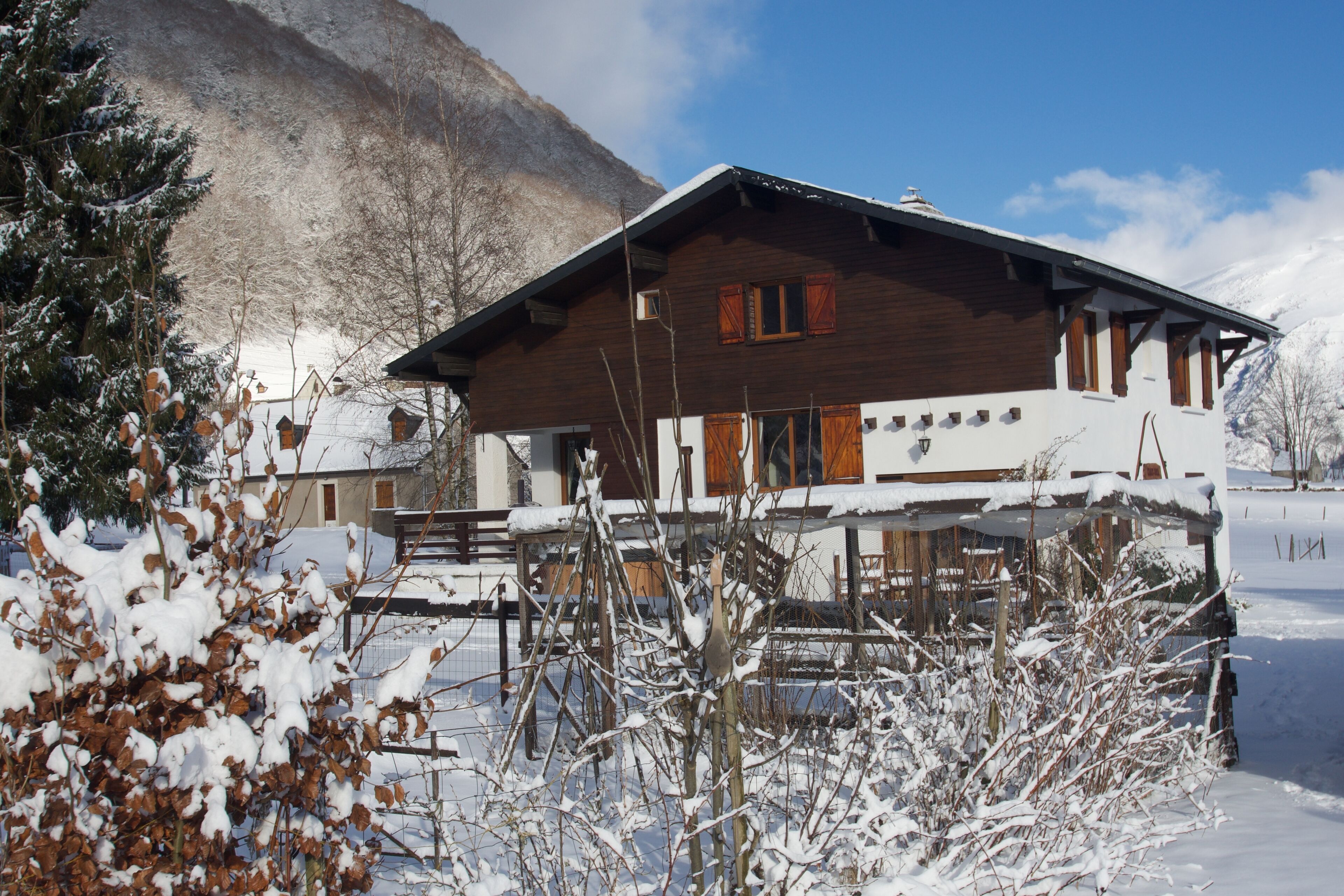 Eine Holzhütte mit einem Balkon, umgeben von schneebedeckten Bäumen und einem Berg im Hintergrund.