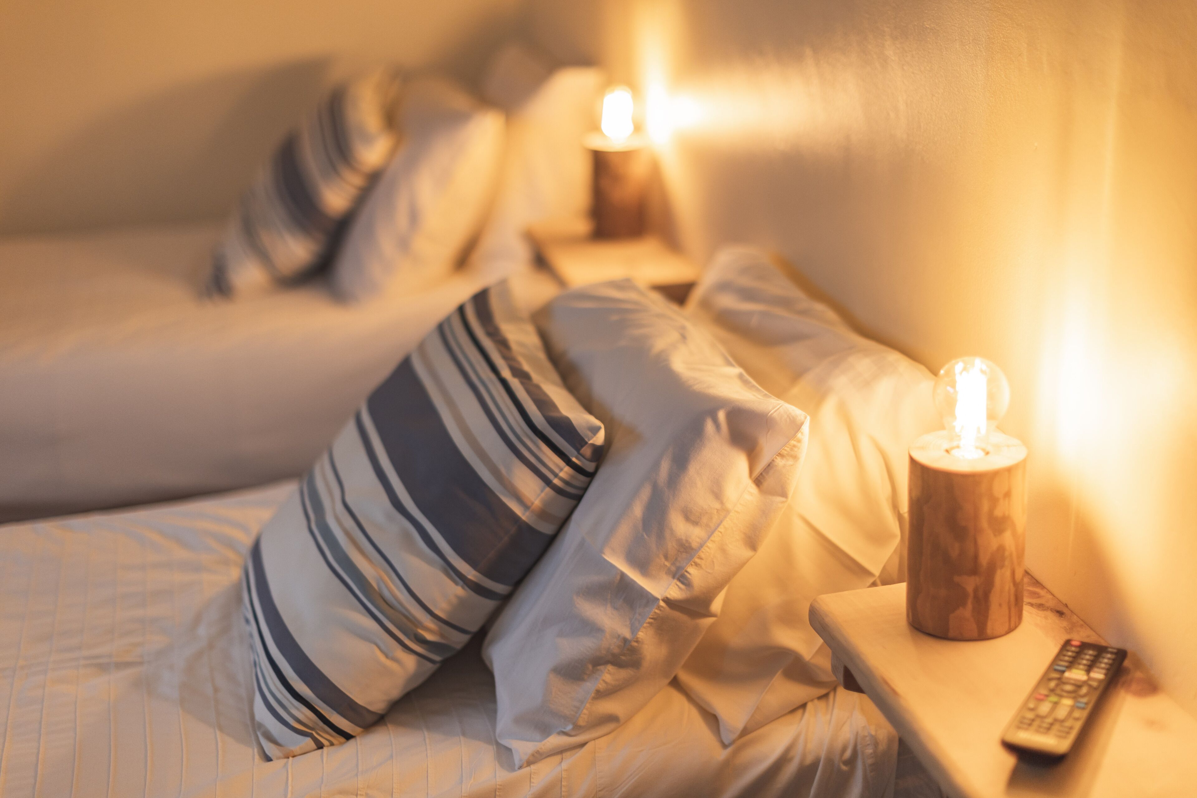 A bedroom with a bed, pillows, a remote control, and a lit candle on a bedside table.