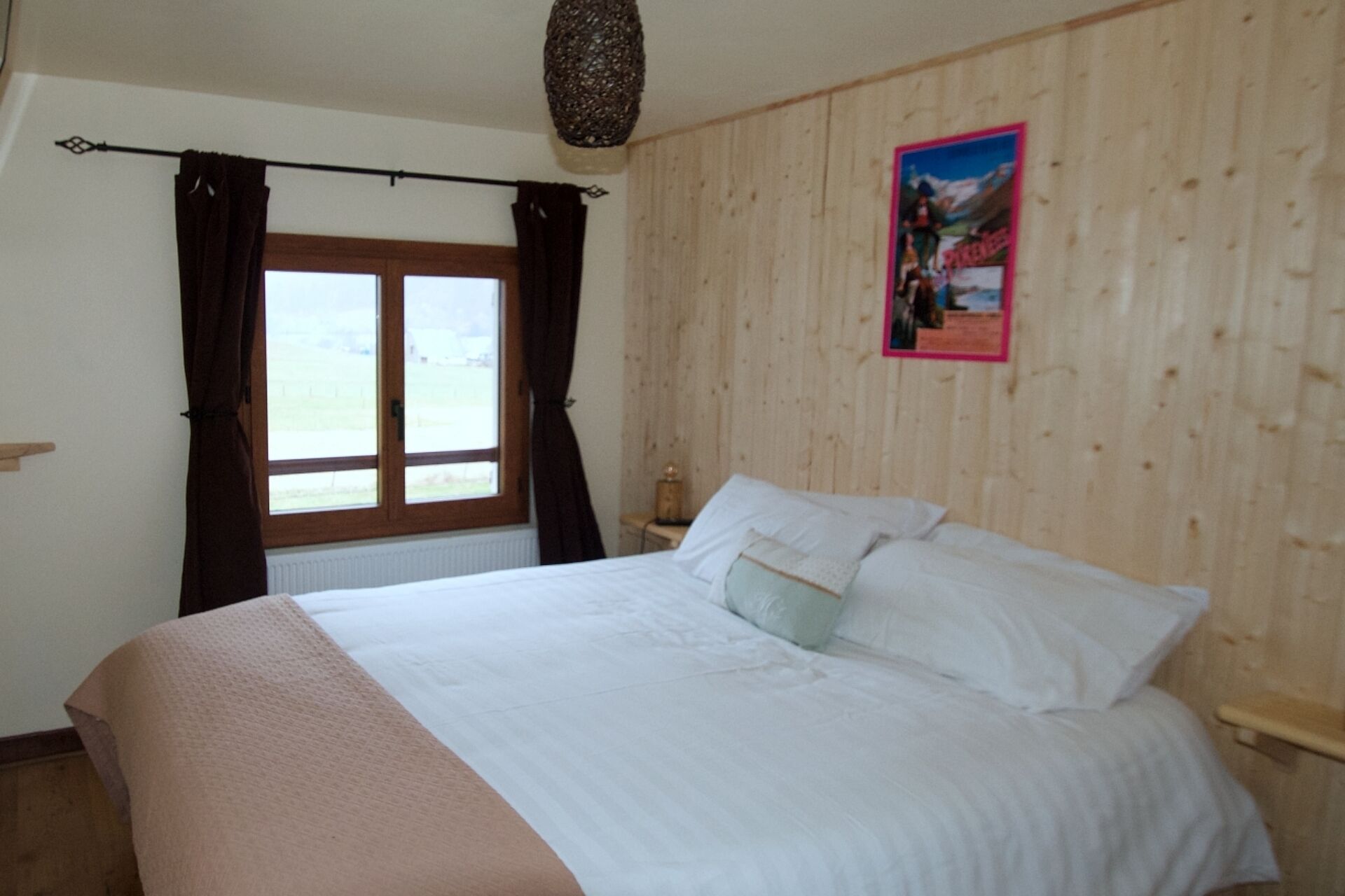 Een slaapkamer met een groot bed, houten wanden, een raam met gordijnen en een poster aan de muur.