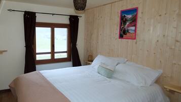 Een slaapkamer met een groot bed, houten wanden, een raam met gordijnen en een poster aan de muur.