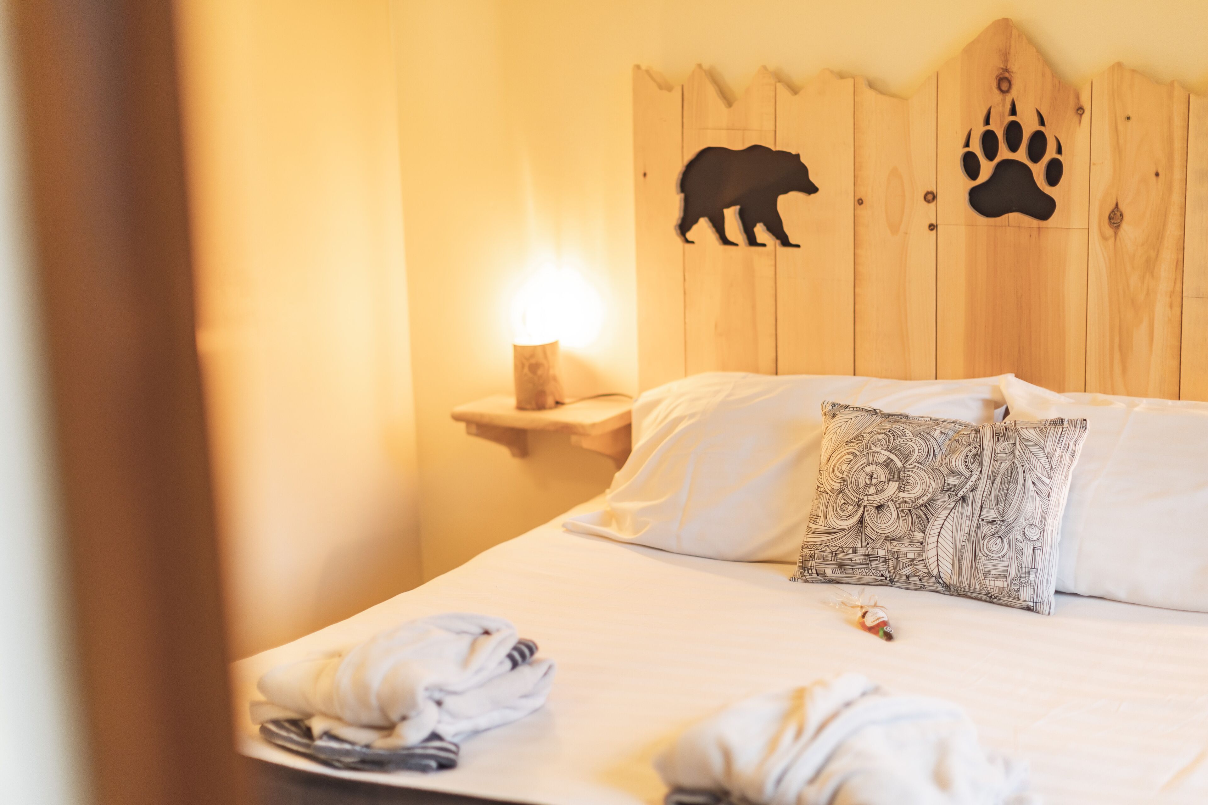 Habitación de hotel con una cama, una mesita de noche con lámpara e impresión de huellas de oso en la pared.