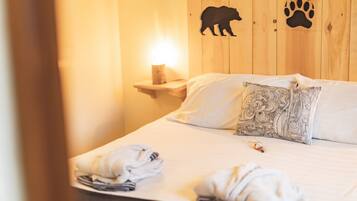 Habitación de hotel con una cama, una mesita de noche con lámpara e impresión de huellas de oso en la pared.