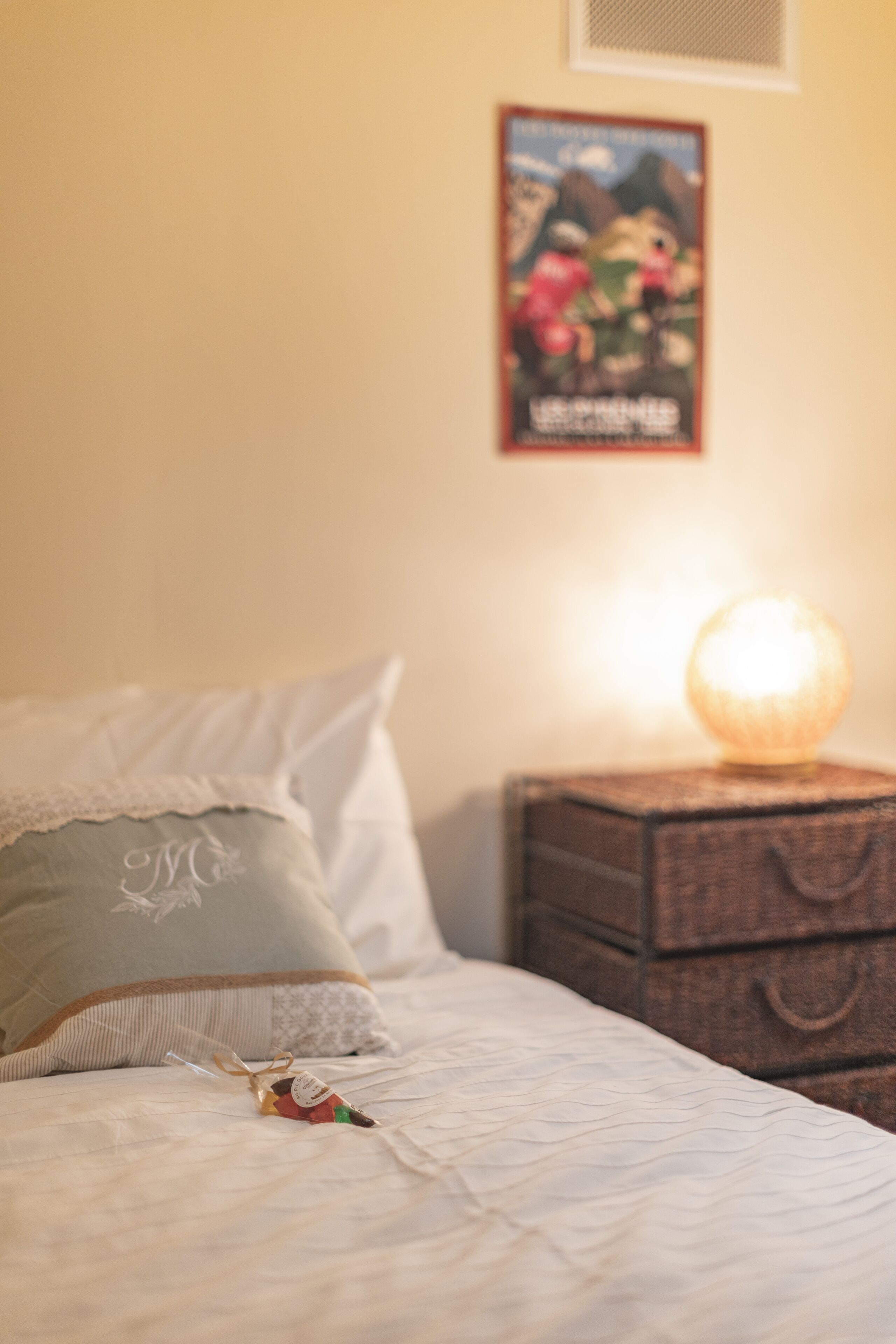 A neatly made bed with a decorative pillow and a small gift box, a bedside lamp, and a framed picture on the wall.