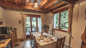 A dining area with a table set for four, wooden chairs, a chandelier, and a view of the outdoors through large windows. - Chalet Ouréa (Campan)