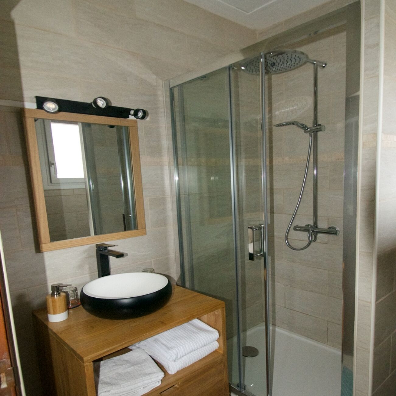 A bathroom with a round sink, a mirror, and a glass-enclosed shower.