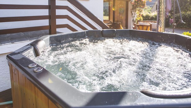 A wooden hot tub with a wooden deck and stairs leading to a building with wooden shutters and a balcony. - Chalet Ouréa (Campan)