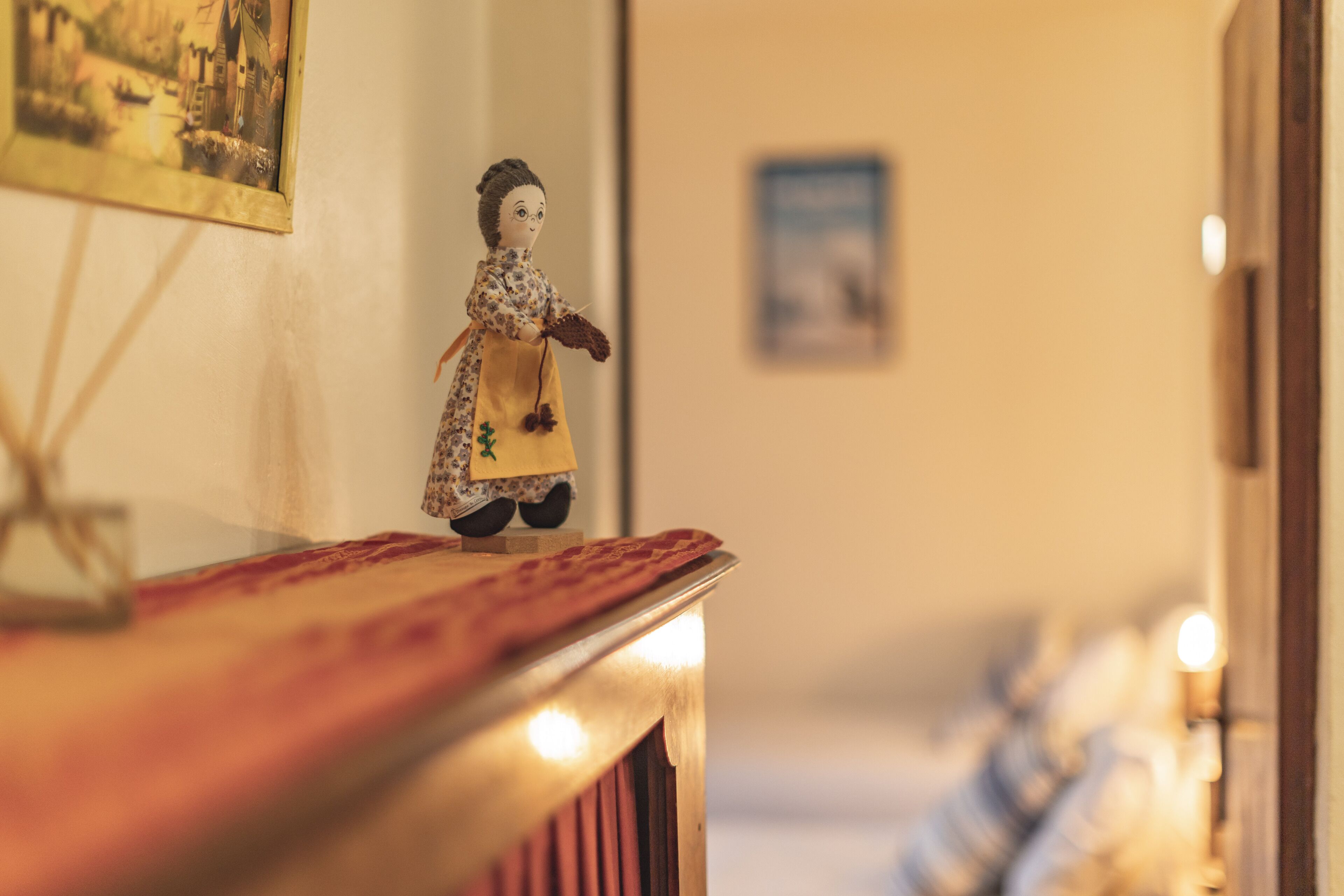 Una muñeca en un estante dentro de una habitación con una cama y un cuadro en la pared.