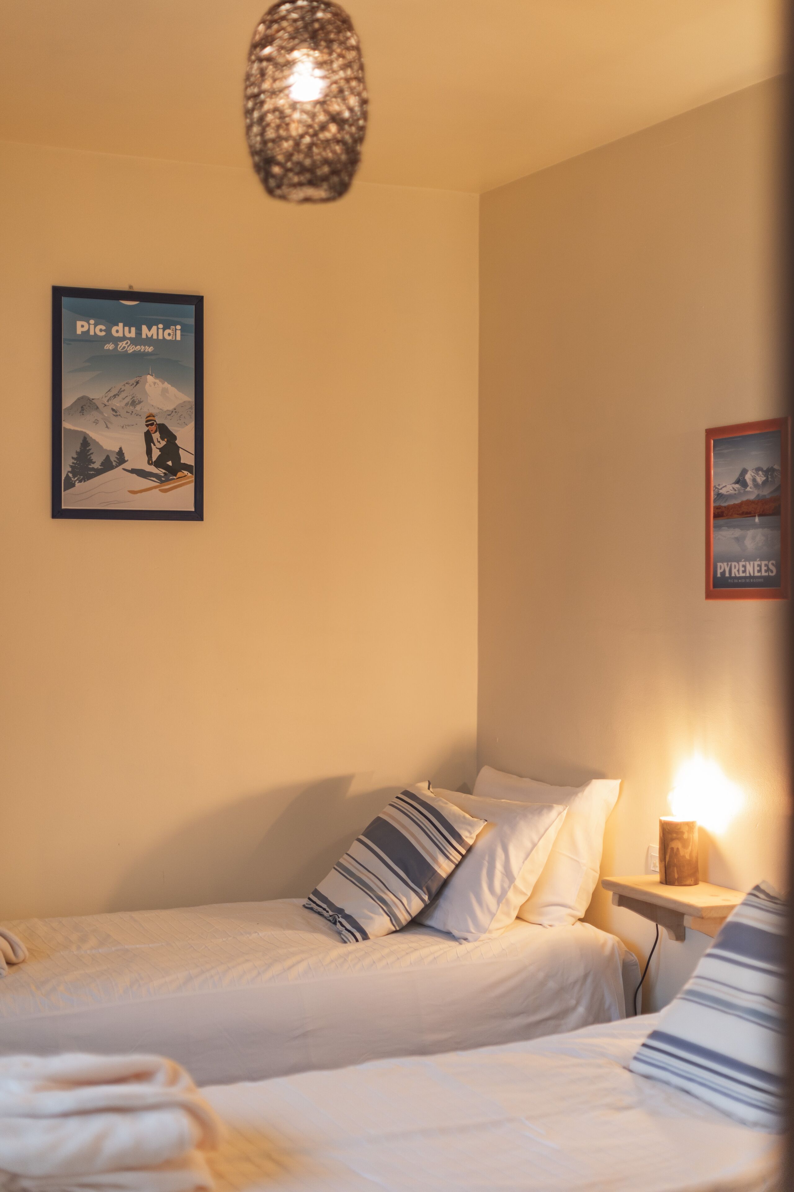 A bedroom with two beds, a wall-mounted light, and two framed pictures.