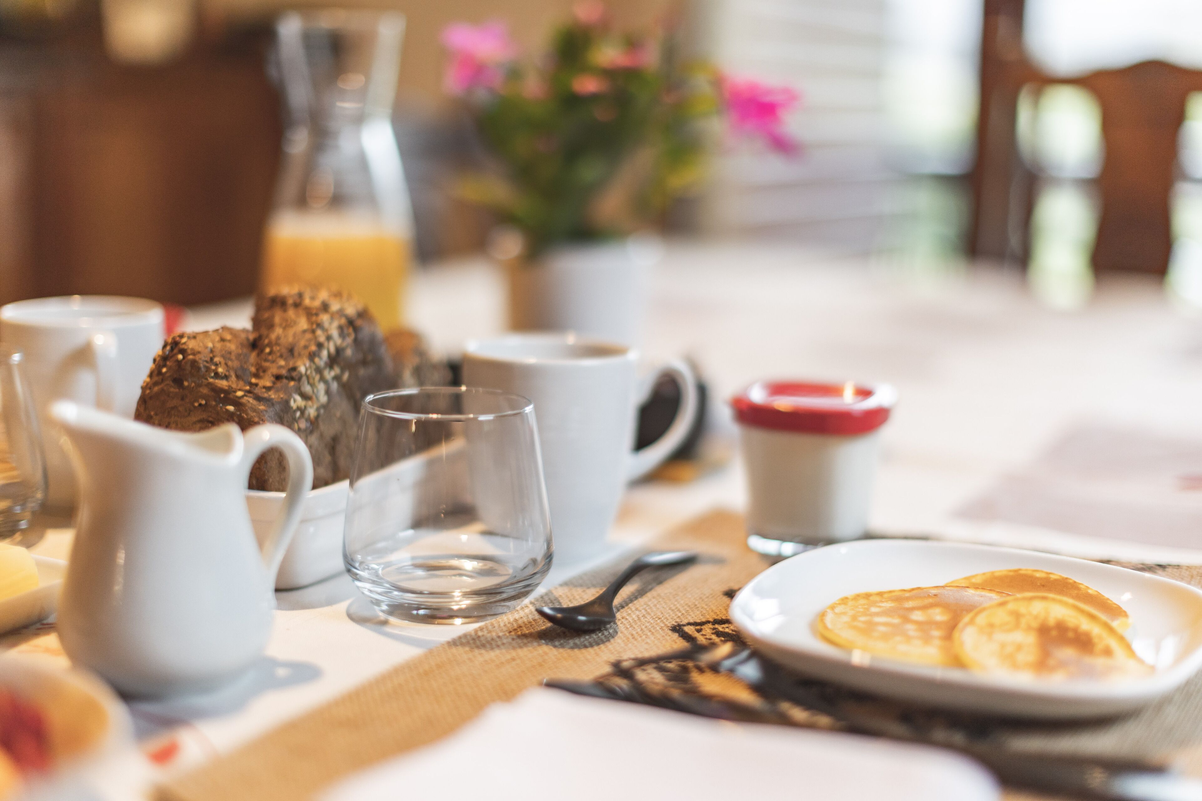 A breakfast table with a plate of pancakes, a pitcher, and a glass.