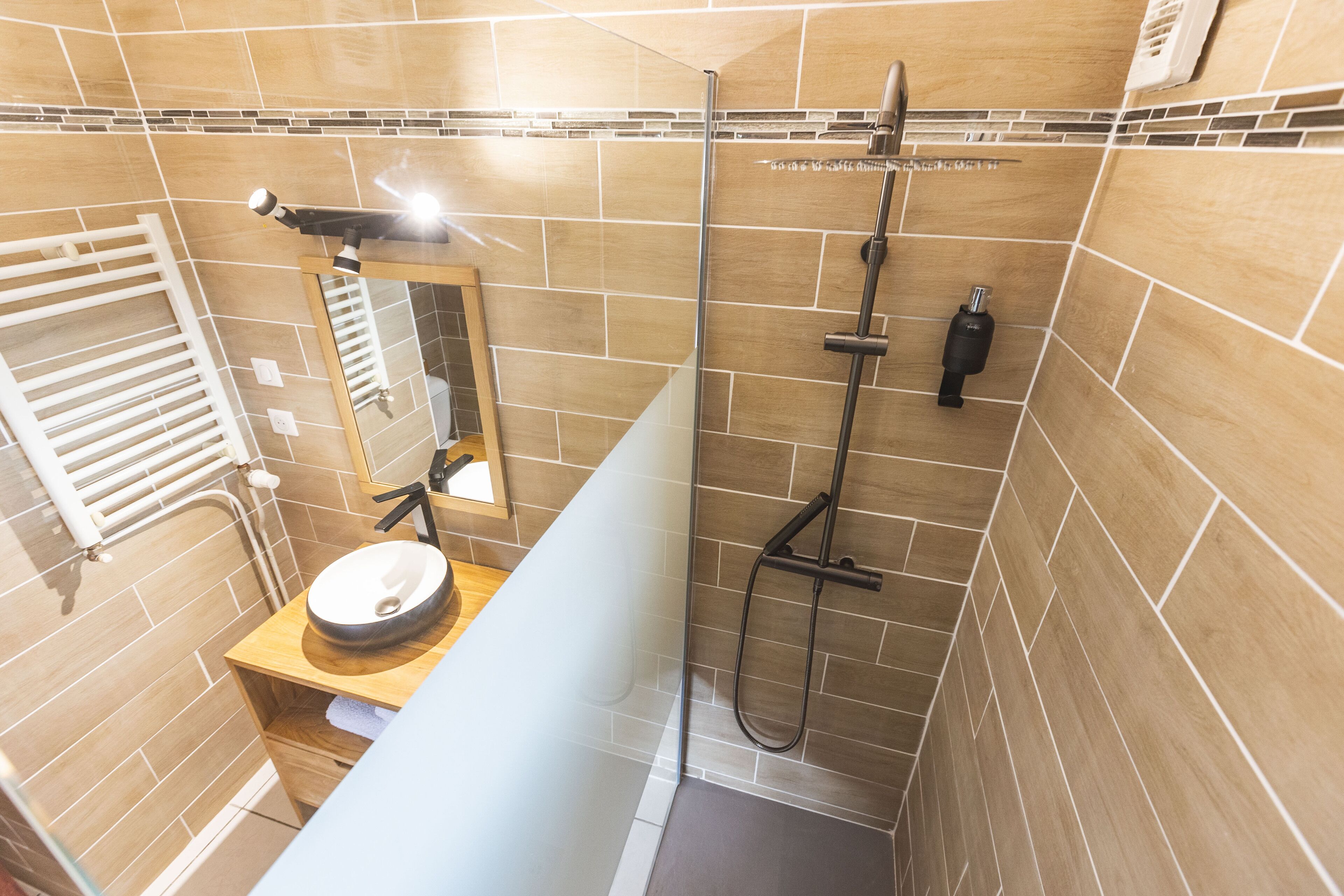 A modern bathroom with a glass shower enclosure, a wooden vanity, and a white towel rack.