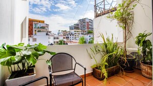 Un balcon avec une chaise, des plantes en pot et une vue sur les immeubles.