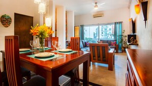 Un coin repas avec une table en bois dressée pour quatre personnes, un vase de fleurs et, en arrière-plan, une vue sur le salon.