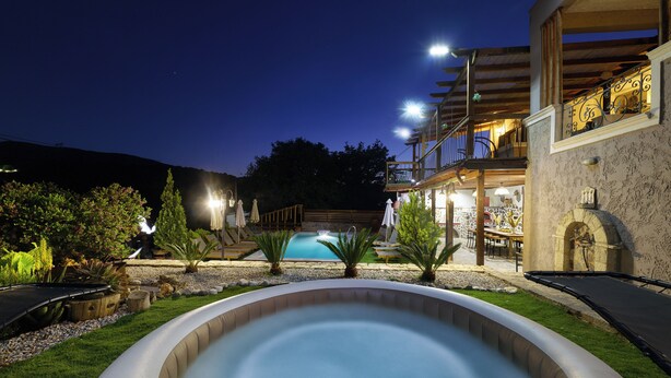 A swimming pool with a hot tub, surrounded by a landscaped garden with various plants and a wooden deck. - Villa Fisi 1 - Pool, Hot Tub & Mountain View (Mylopotamos)