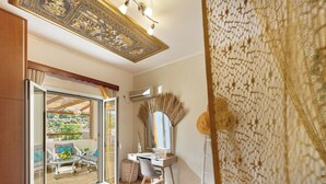 A room with a large sliding glass door leading to an outdoor seating area, a white vanity with a mirror, and a ceiling with intricate patterns. - Villa Fisi 1 - Pool, Hot Tub & Mountain View (Mylopotamos)