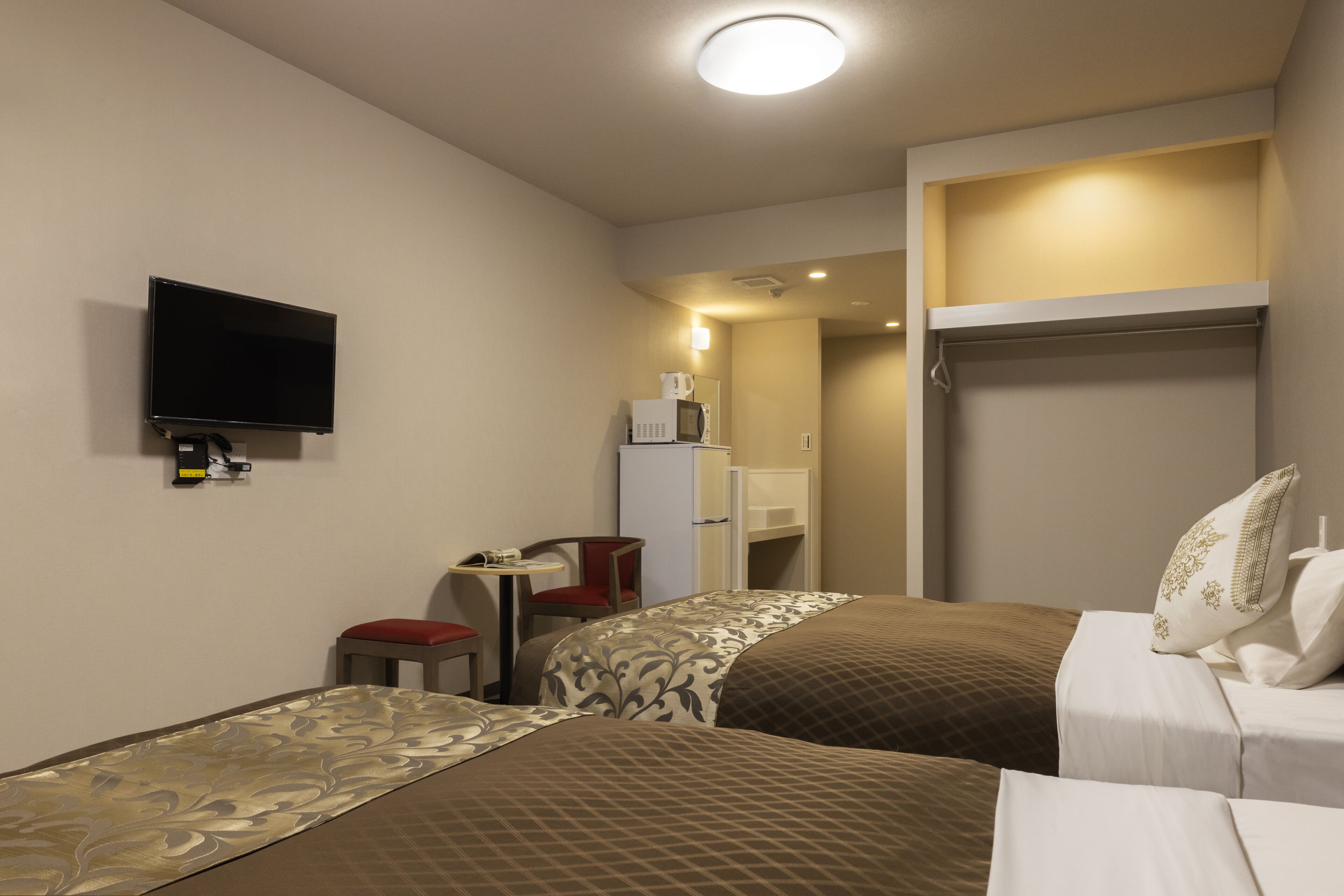 A hotel room with two beds, a television, a desk with a chair, a microwave, and a wardrobe.