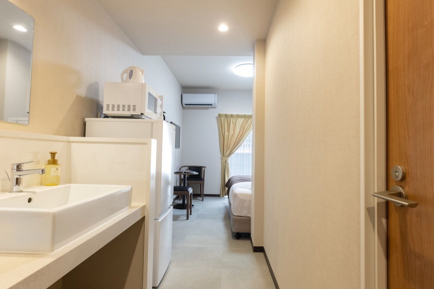 A narrow hotel corridor with a sink, mirror, and a small table with chairs.