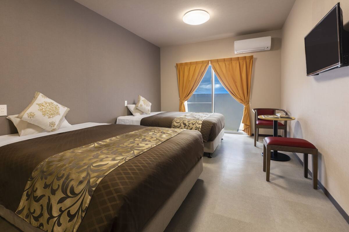 A hotel room with two beds, a desk, and a chair.