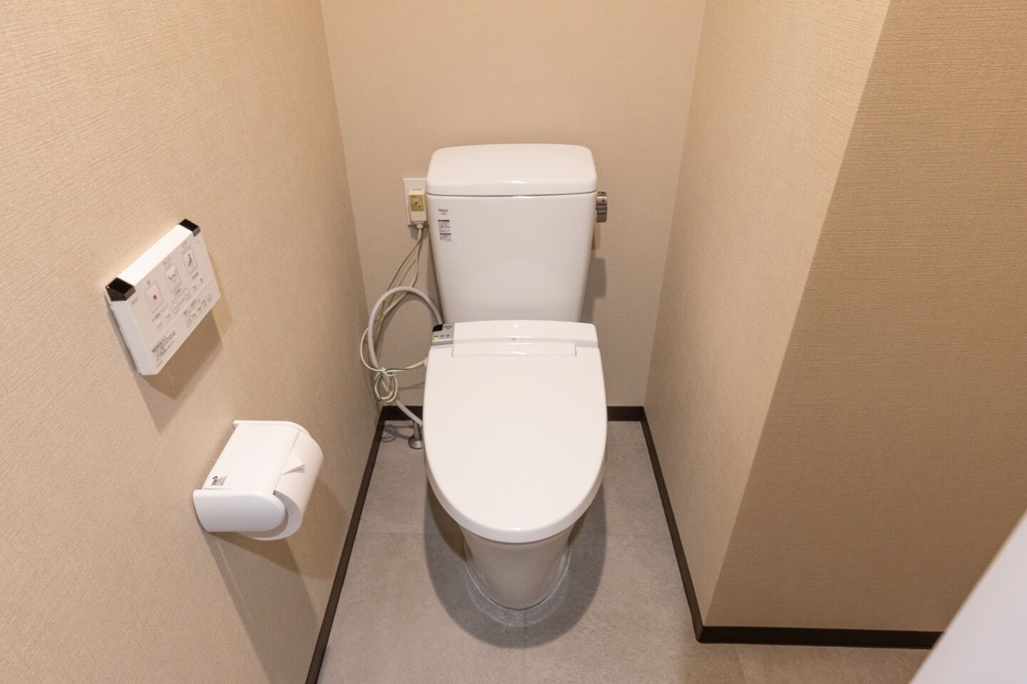 Een kleine, schone badkamer met toilet, handdroger en een papieren handdoekdispenser.