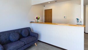 A reception area with a wooden counter, a blue sofa, and a small vase with flowers. - Mr.KINJO Miyakojima Aparagi Resort 1 (Miyakojima)