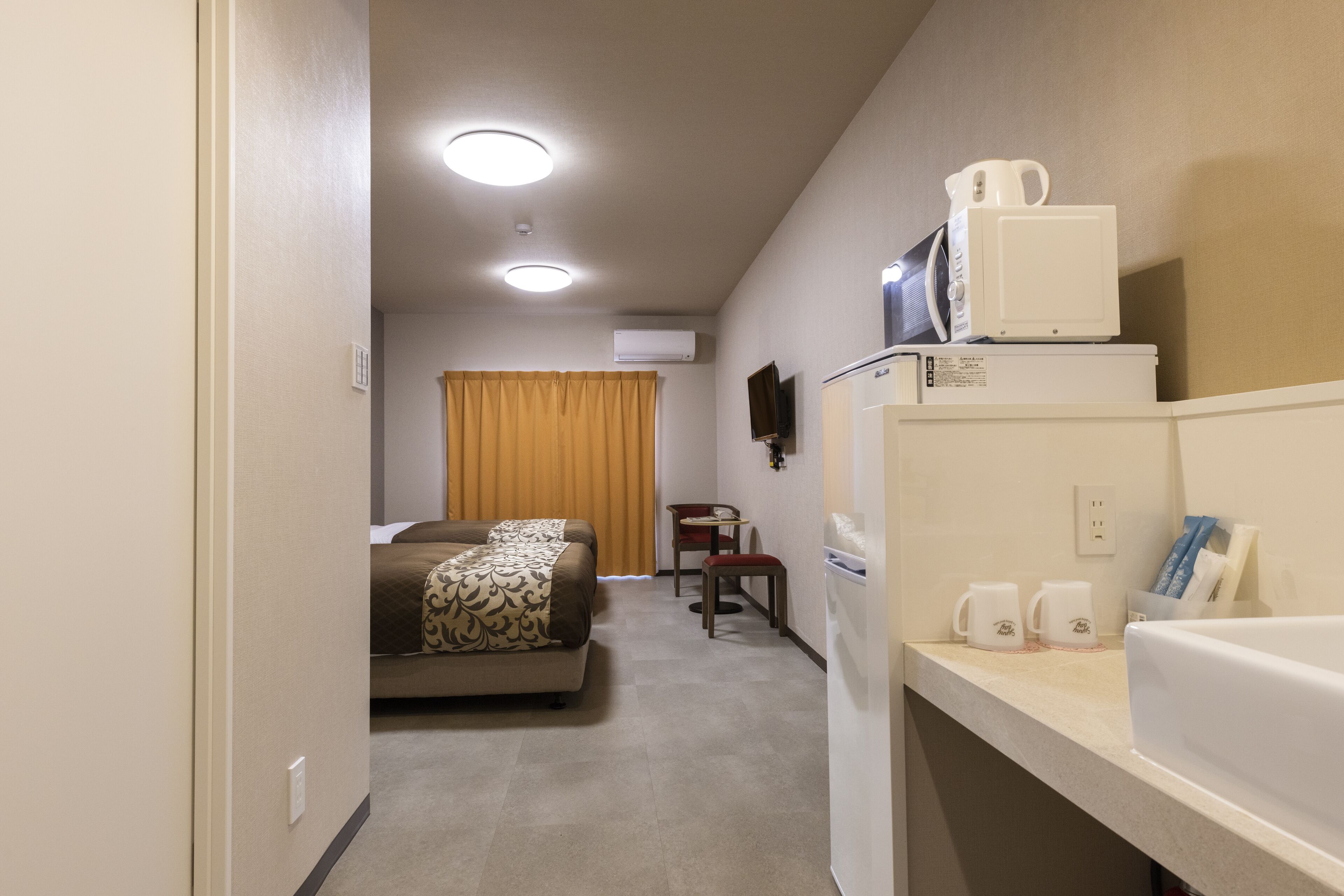 A hotel room with a bed, a small table with a chair, a microwave, a refrigerator, and a television on the wall.