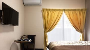 Habitación de hotel con cama, televisión montada en la pared, una silla y una mesita con un libro.