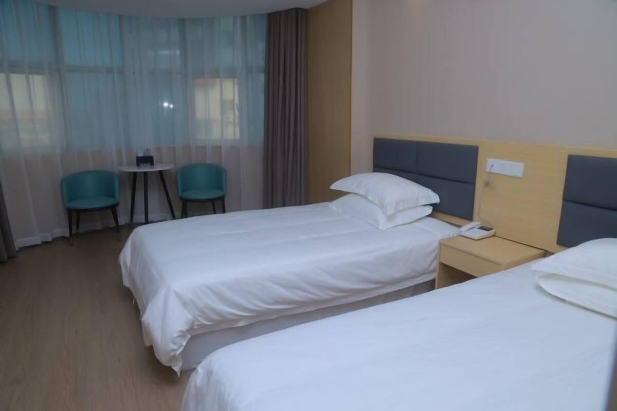 Ein Hotelzimmer mit zwei Einzelbetten, einem kleinen Tisch mit Stühlen und einem Fenster mit durchsichtigen Vorhängen.