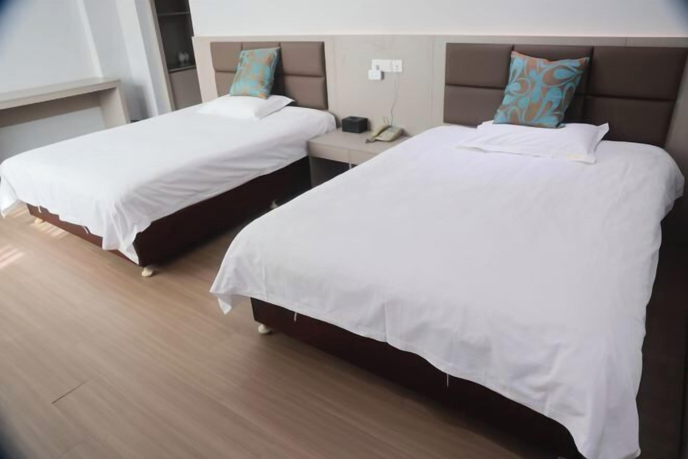 Deux lits simples avec du linge de lit blanc et des coussins décoratifs, un téléphone sur la table de chevet et un plancher en bois.