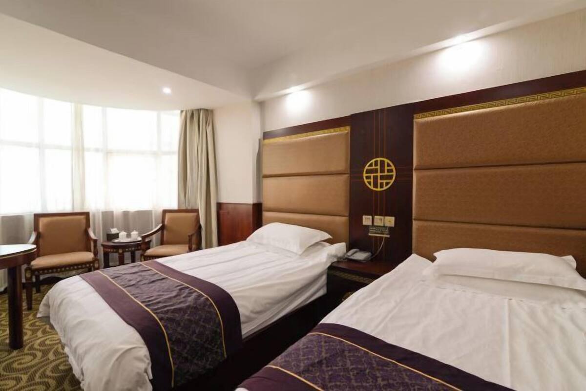 Ein Hotelzimmer mit zwei Betten, einem Schreibtisch, Stühlen und einem großen Fenster.