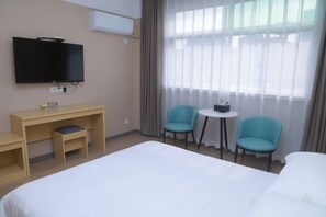 Habitación de hotel con cama, escritorio, dos sillas, una mesita y televisión.
