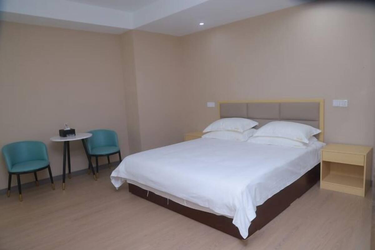 Ein Hotelzimmer mit einem großen Bett, zwei Sesseln, einem kleinen Tisch und einem Nachttisch.