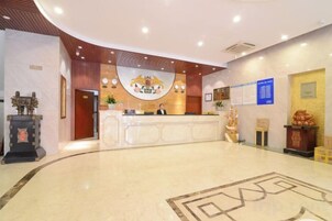 Zona de recepción de hotel con un mostrador curvo, un emblema en la pared y un tablón de anuncios.