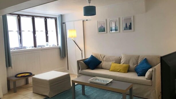 A living room with a sofa, ottoman, coffee table, floor lamp, and a window with curtains. - "L'Historique": House 2 minutes' walk from the center (Bayeux)