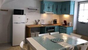 A compact kitchen with teal cabinets, a white refrigerator, and a dining table with chairs. - "L'Historique": House 2 minutes' walk from the center (Bayeux)