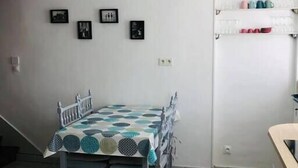 A dining area with a table set for four, a white wall with three framed pictures, and a white door with a shelf above it.