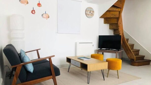 A modern living room with a sofa, coffee table, and TV. There's a wooden staircase and a white door.