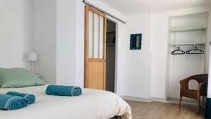 A bedroom with a bed, a wooden door, a chair, and a wardrobe with hangers.