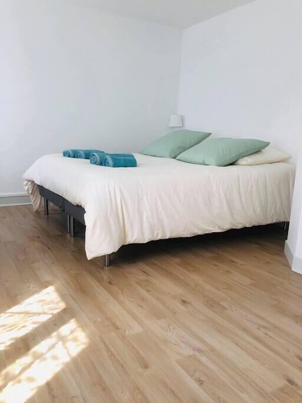 Un dormitorio con cama, almohadas y una colcha enrollada.
