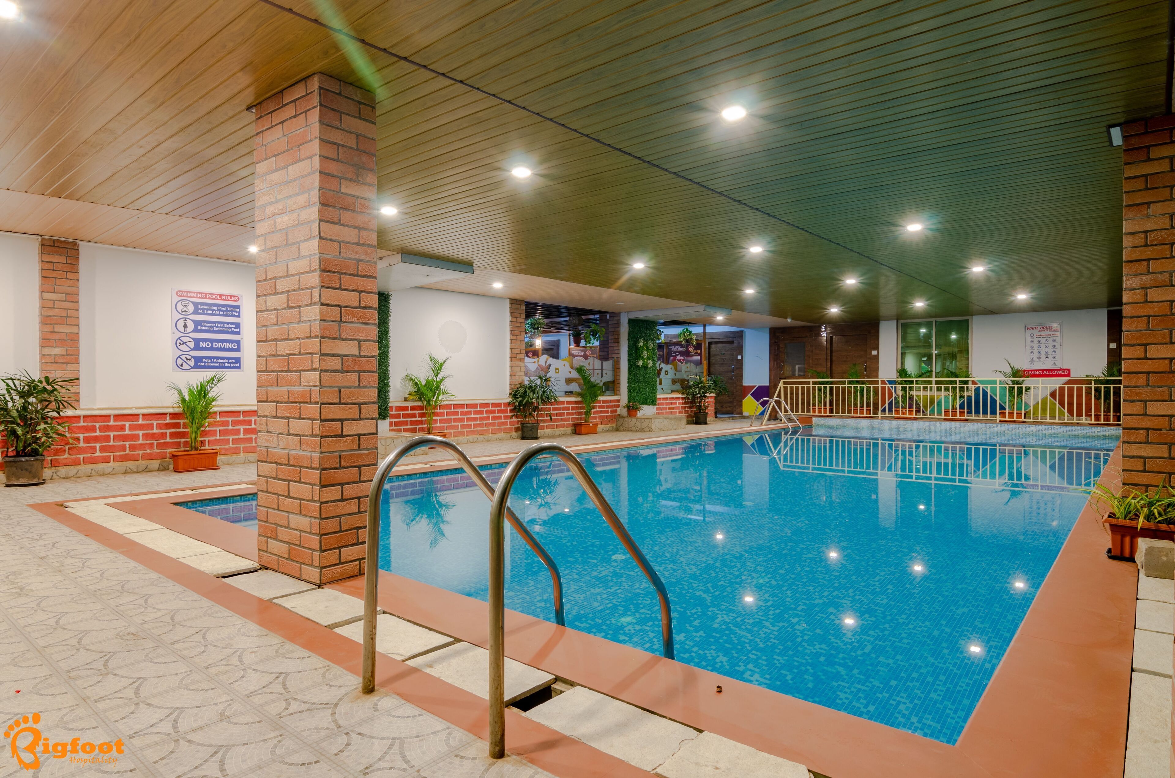 Una piscina interior con suelo de baldosas, escalera metálica y pilares de ladrillo.