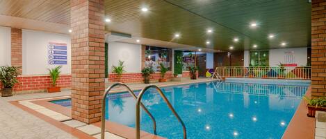 An indoor swimming pool with a tiled floor, metal pool ladder, and brick pillars.