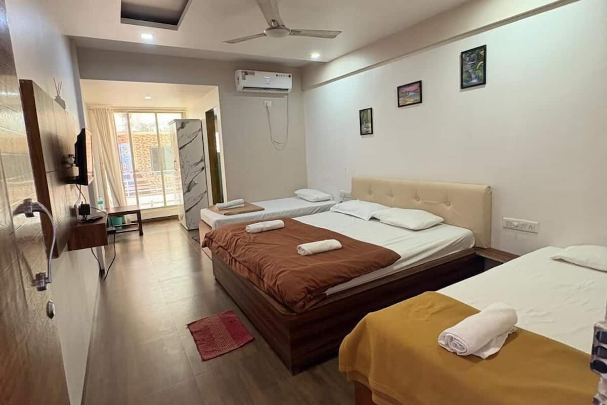 Habitación de hotel con dos camas, ventilador de techo, equipo de aire acondicionado y una pequeña mesa con una silla.