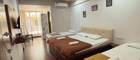 Habitación de hotel con dos camas, ventilador de techo, equipo de aire acondicionado y una pequeña mesa con una silla.