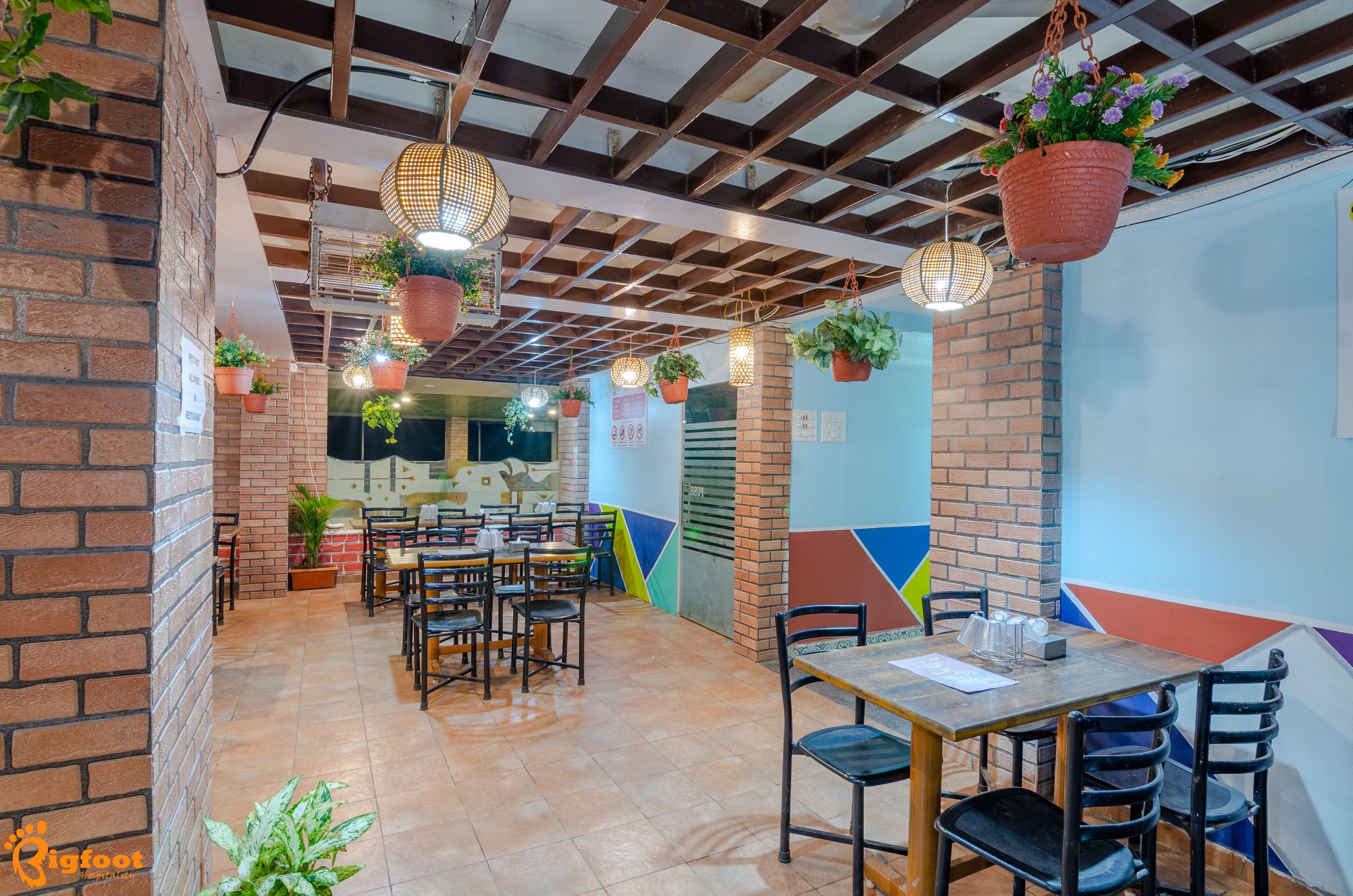 A restaurant with brick walls, hanging plants, and a colorful geometric wall design.